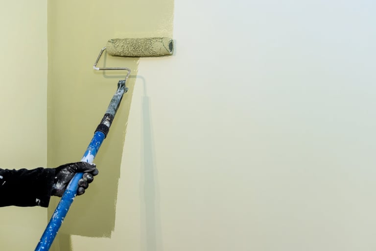 Carpenter paints wall with roller, working on home renovation project in bright living area