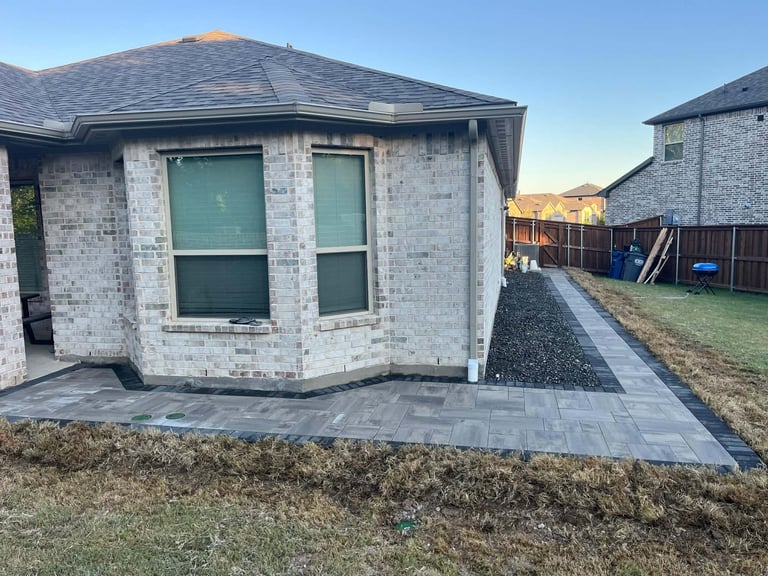 New brick residential home exterior with stone patio, green doors and windows, under clear blue sky in a suburban neighborhood